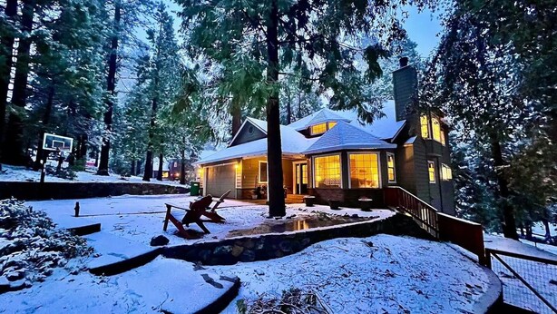A snow-covered landscape with a house featuring a large garage and a stone retaining wall.