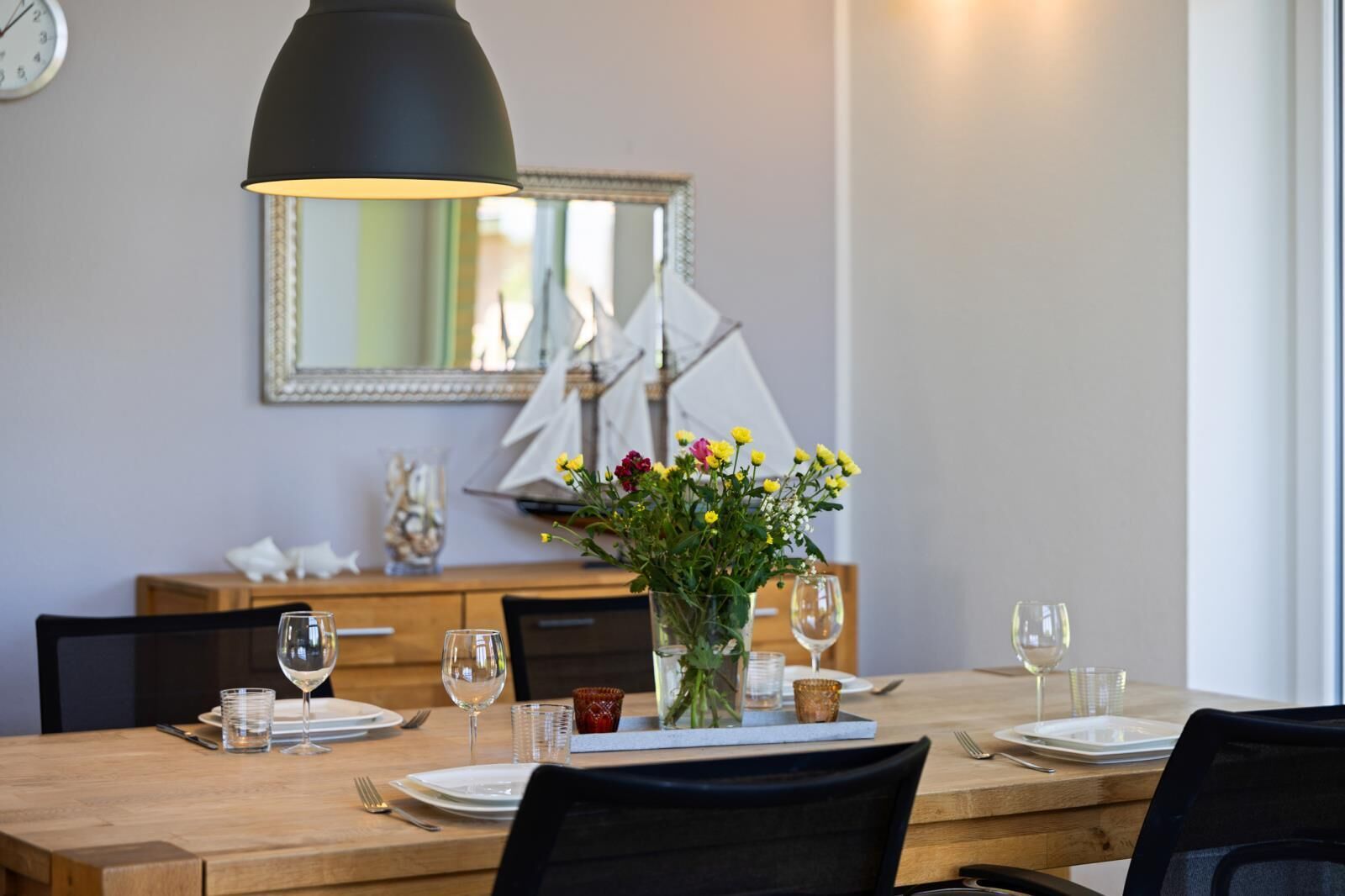 Een eettafel gedekt met borden, glazen en een vaas met bloemen.
