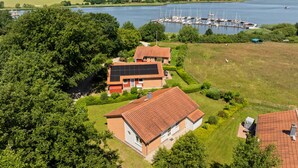 Zona residencial con una casa que tiene paneles solares, un muelle con barcos y una extensa masa de agua al fondo.
