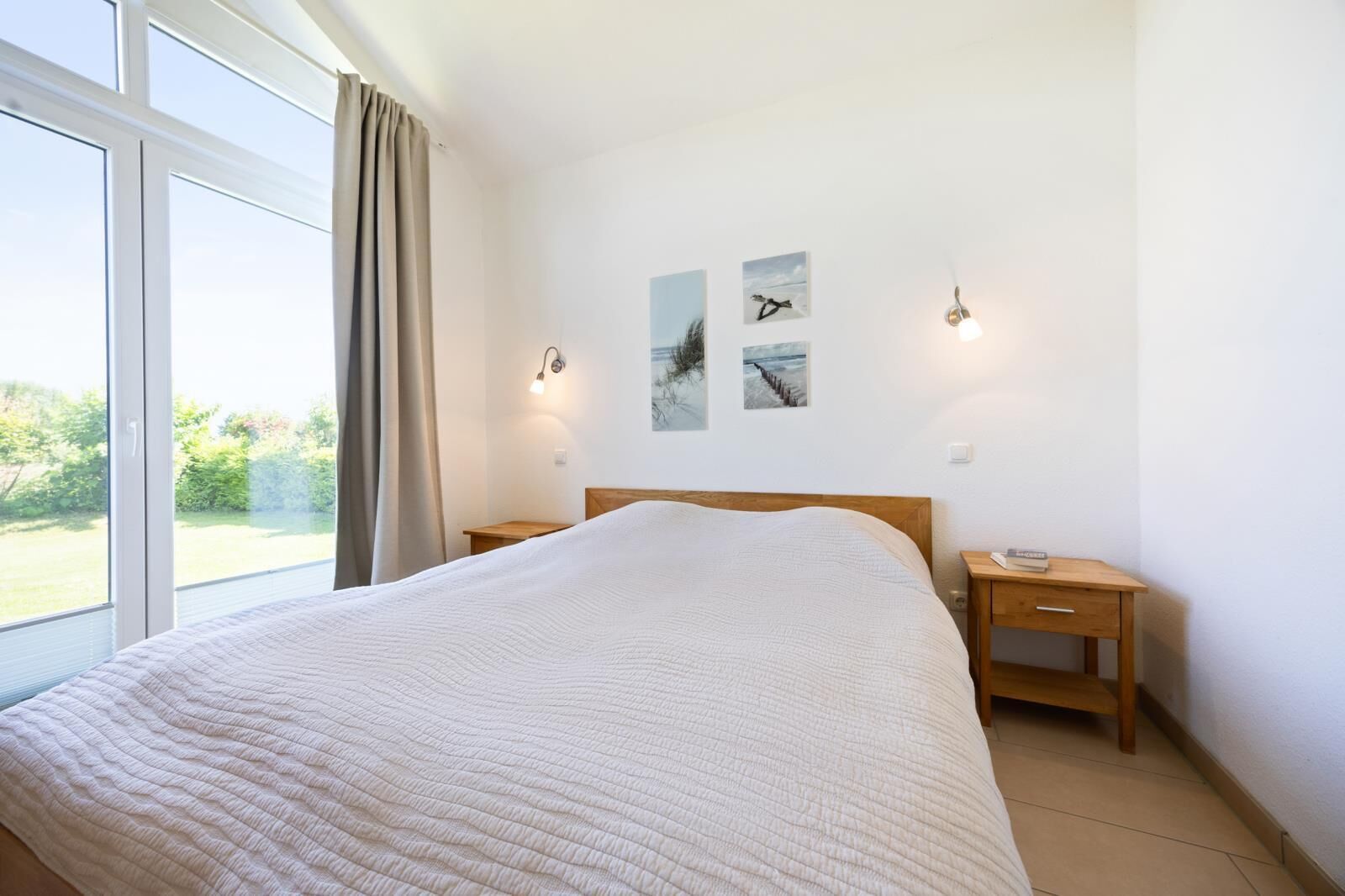 Quarto com uma cama grande, duas mesinhas de cabeceira, um criado-mudo e uma janela com cortinas.