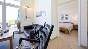 Una sala moderna con un sofá de cuero, una mesa de comedor y vistas a un dormitorio con cama y obras de arte.