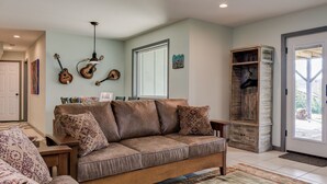 A living room with a sofa, a coffee table, and a rug. There are guitars on the wall and a wooden cabinet with a hanging rack. - Pets welcomed, fully fenced in yard. Beautiful 1BR suite w full kitchen, WI-FI  (Candler)