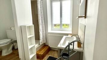 Un bagno compatto con il water, un lavandino, una finestra e un piccolo gradino che conduce alla zona doccia.