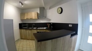 Une cuisine de taille réduite, avec des meubles en bois, un plan de travail noir, une cuisinière à gaz et une horloge murale.