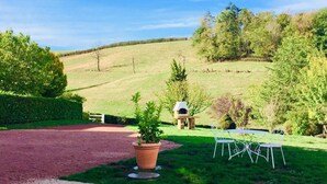 Un paysage rural avec un ciel dégagé, un chemin de gravier, une plante en pot, un four en pierre et une table en métal avec des chaises.