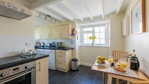 Una cocina moderna con lavavajillas, horno y microondas. Hay una mesa de comedor con alimentos para el desayuno y una ventana con vistas al jardín.