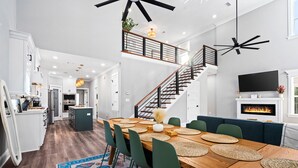 A spacious kitchen with modern appliances, a dining area with a wooden table and green chairs, and a staircase leading to an upper level. - Outdoor Kitchen - Walk to Beach - Fire Pit - Dogs (Gulfport)