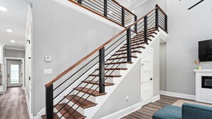 A modern staircase with wooden steps and black railings, leading to a living area with a blue sofa and a fireplace. - Outdoor Kitchen - Walk to Beach - Fire Pit - Dogs (Gulfport)