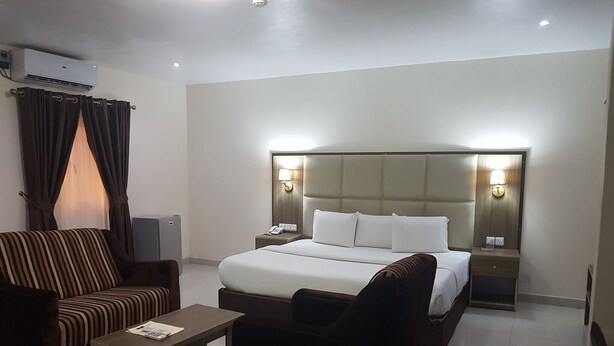 Ein Hotelzimmer mit einem großen Bett, zwei Nachttischen mit Lampen, einem Sofa, einem Couchtisch und einer Klimaanlage.