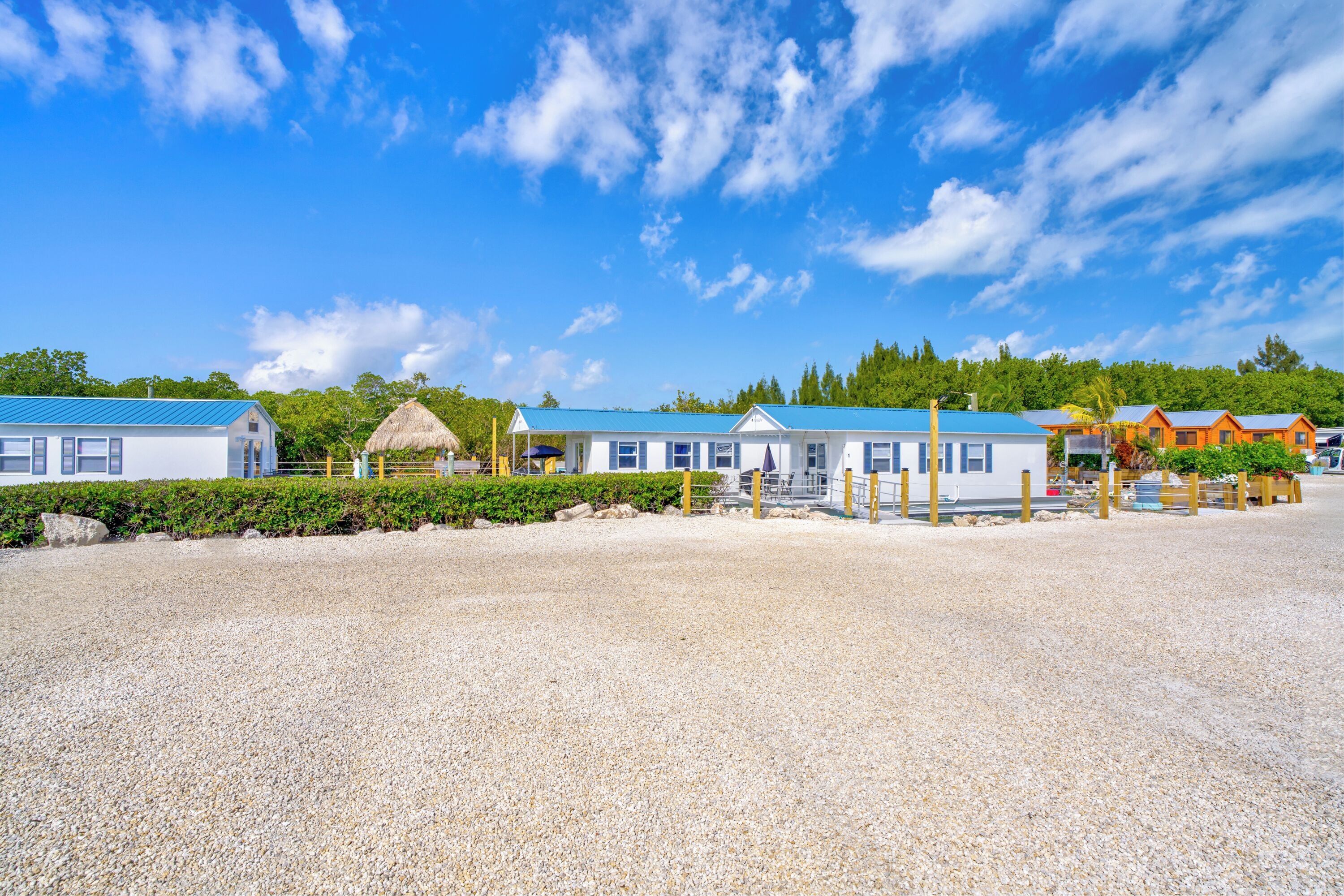 A beachfront property with multiple cabins, a thatched-roof structure, and a gravel beach.
