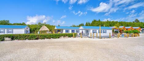 A beachfront property with multiple cabins, a thatched-roof structure, and a gravel beach.