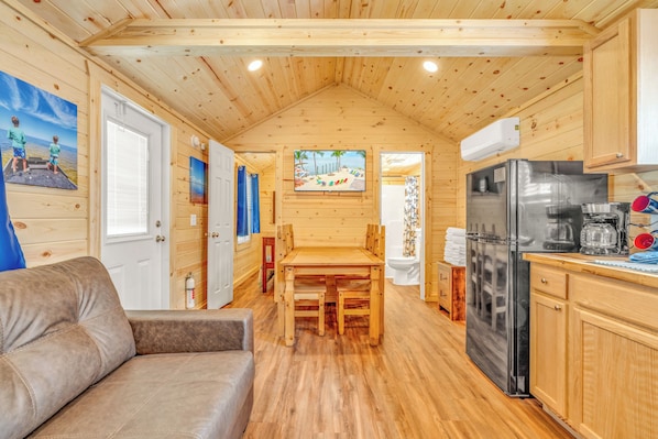 Uma cabana de madeira compacta com área de jantar, cozinha e sofá.