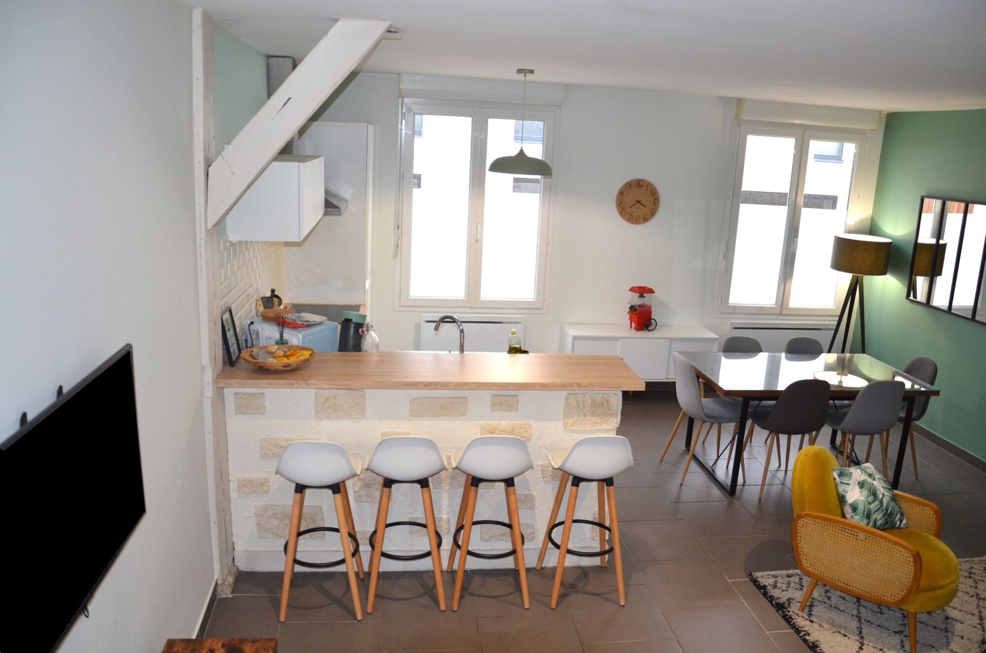 Una cucina moderna con isola centrale, sgabelli da bar, un tavolo da pranzo con sedie e una scala.