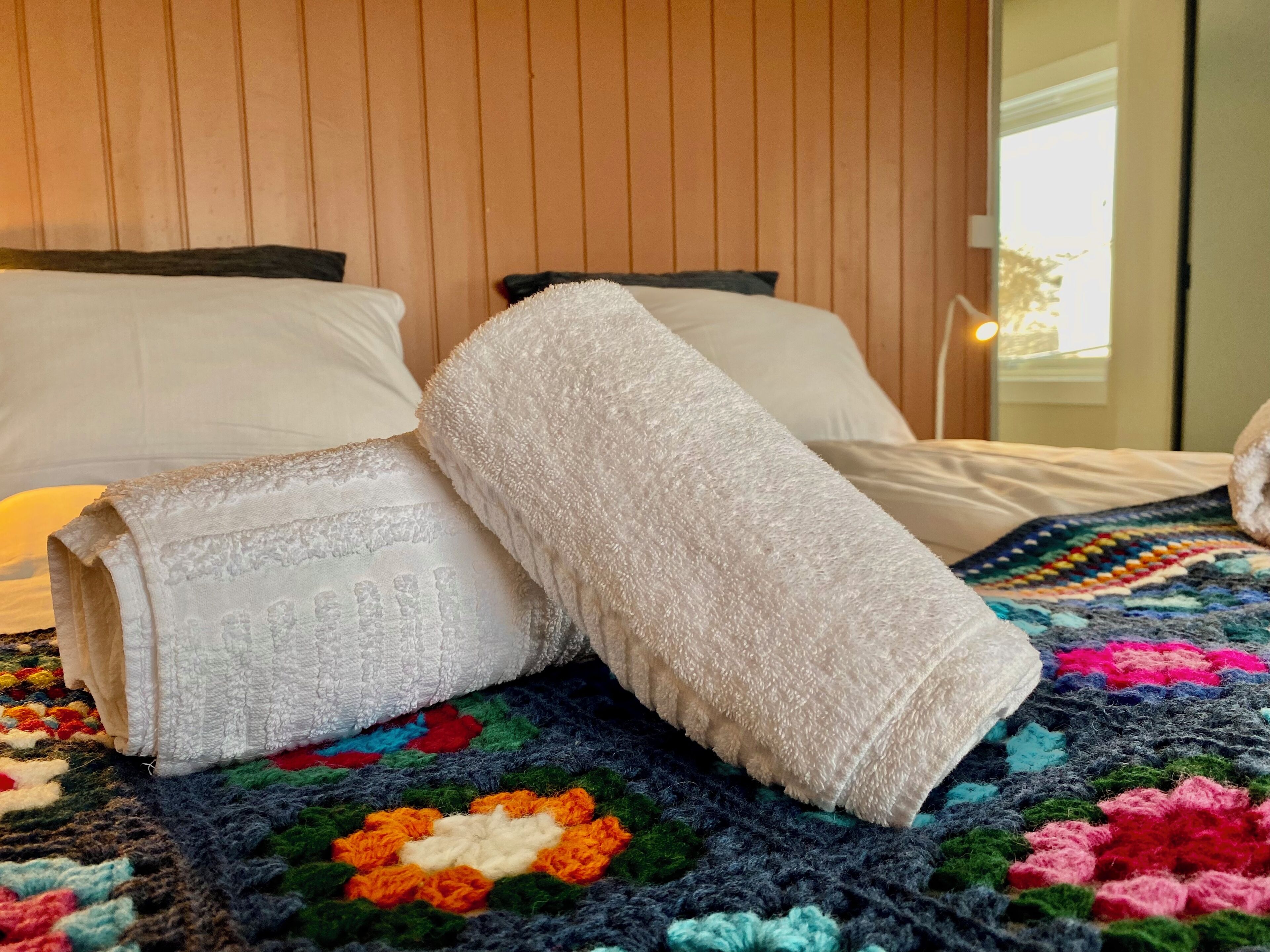 A bed with white linens, a colorful crocheted blanket, and a wooden headboard.