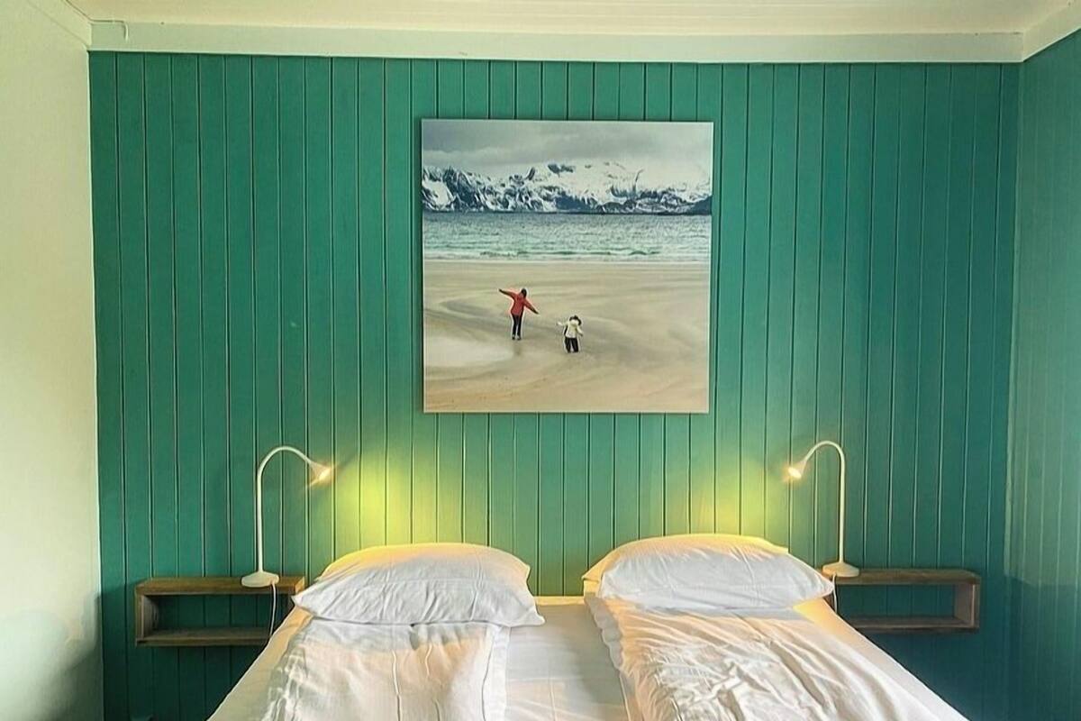 A room with a bed, two bedside tables, and a painting of a snowy beach scene.
