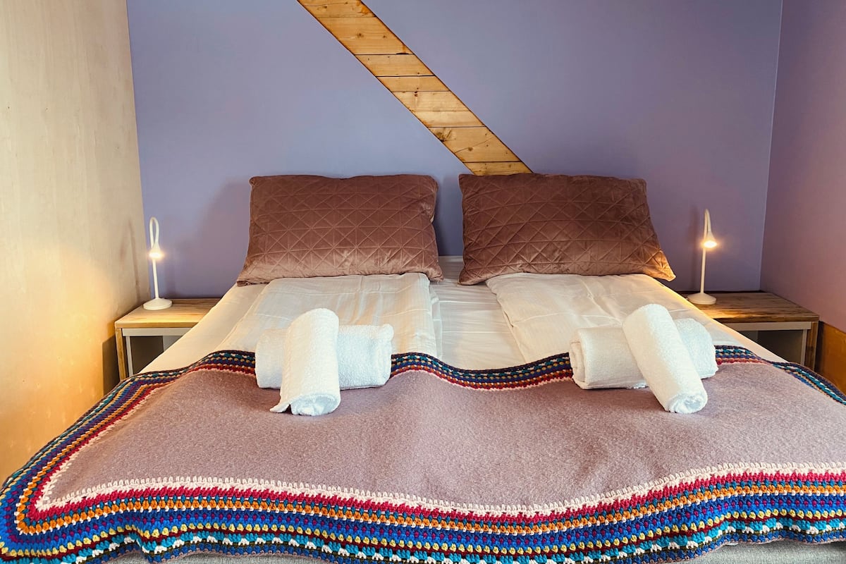 A double bed with two brown pillows, a colorful blanket, and two bedside lamps.