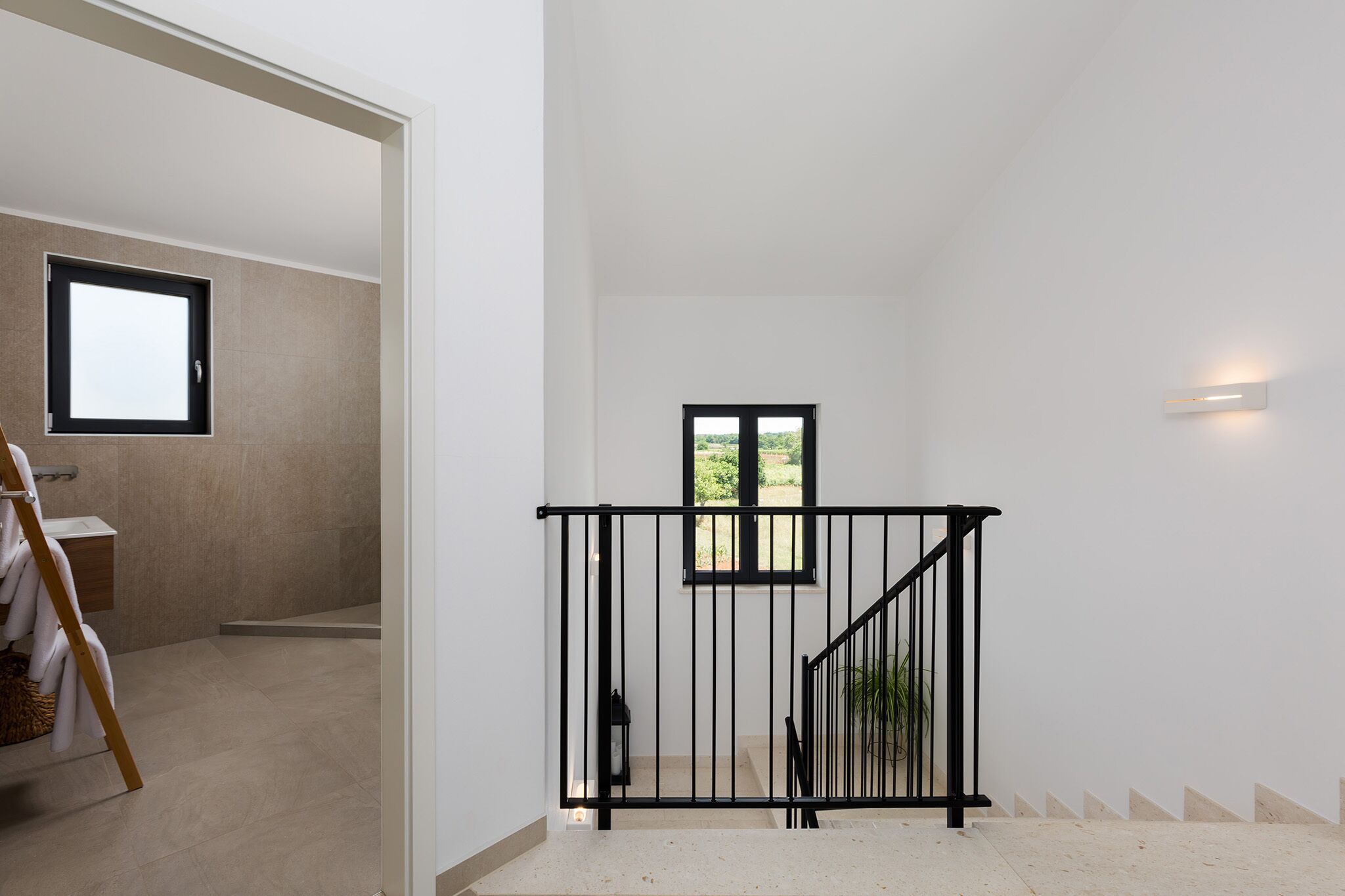A modern interior with a staircase, a small window, and a wall-mounted light fixture.