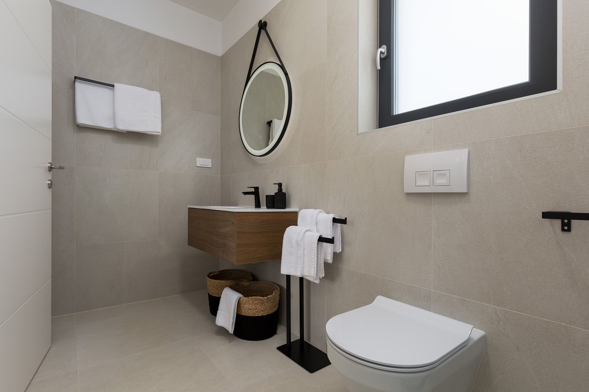 A modern bathroom with a toilet, sink, and mirror. There are two baskets under the sink and a towel rack with towels.