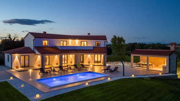 Une maison moderne à deux étages, dotée d’une piscine, d’un espace extérieur aménagé et d’une terrasse bien éclairée.
