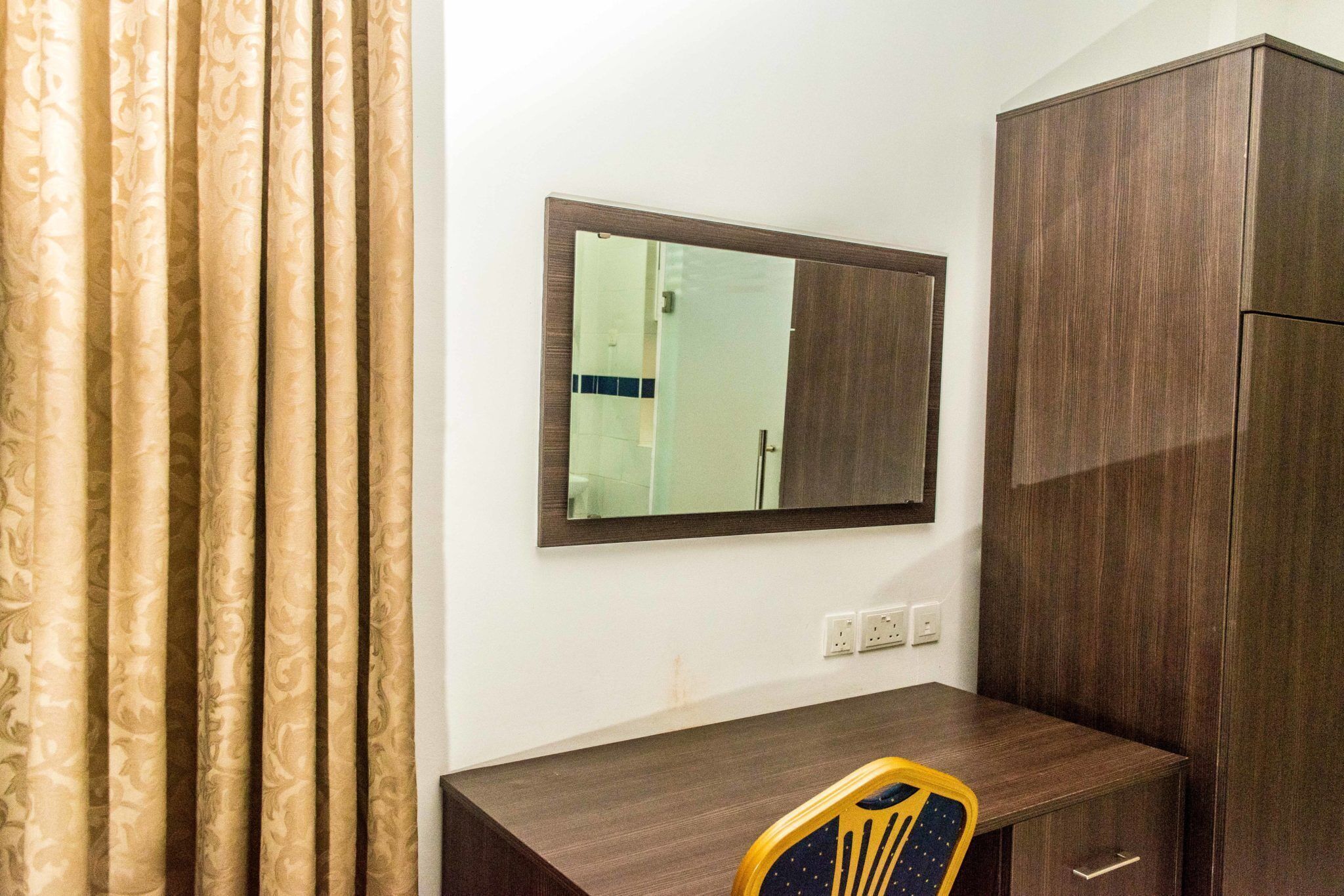 A room with a wooden desk, a mirror, a wardrobe, and a patterned curtain.