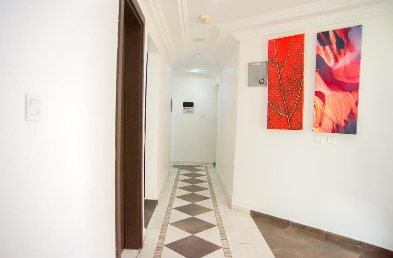 Un couloir doté d’un sol à carreaux, de murs blancs et de deux tableaux abstraits.