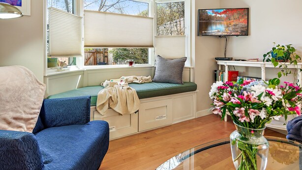 Ein gemütliches Wohnzimmer mit einer eingebauten Bank, einem Flachbildfernseher, einem Bücherregal und einem Blumenstrauß.