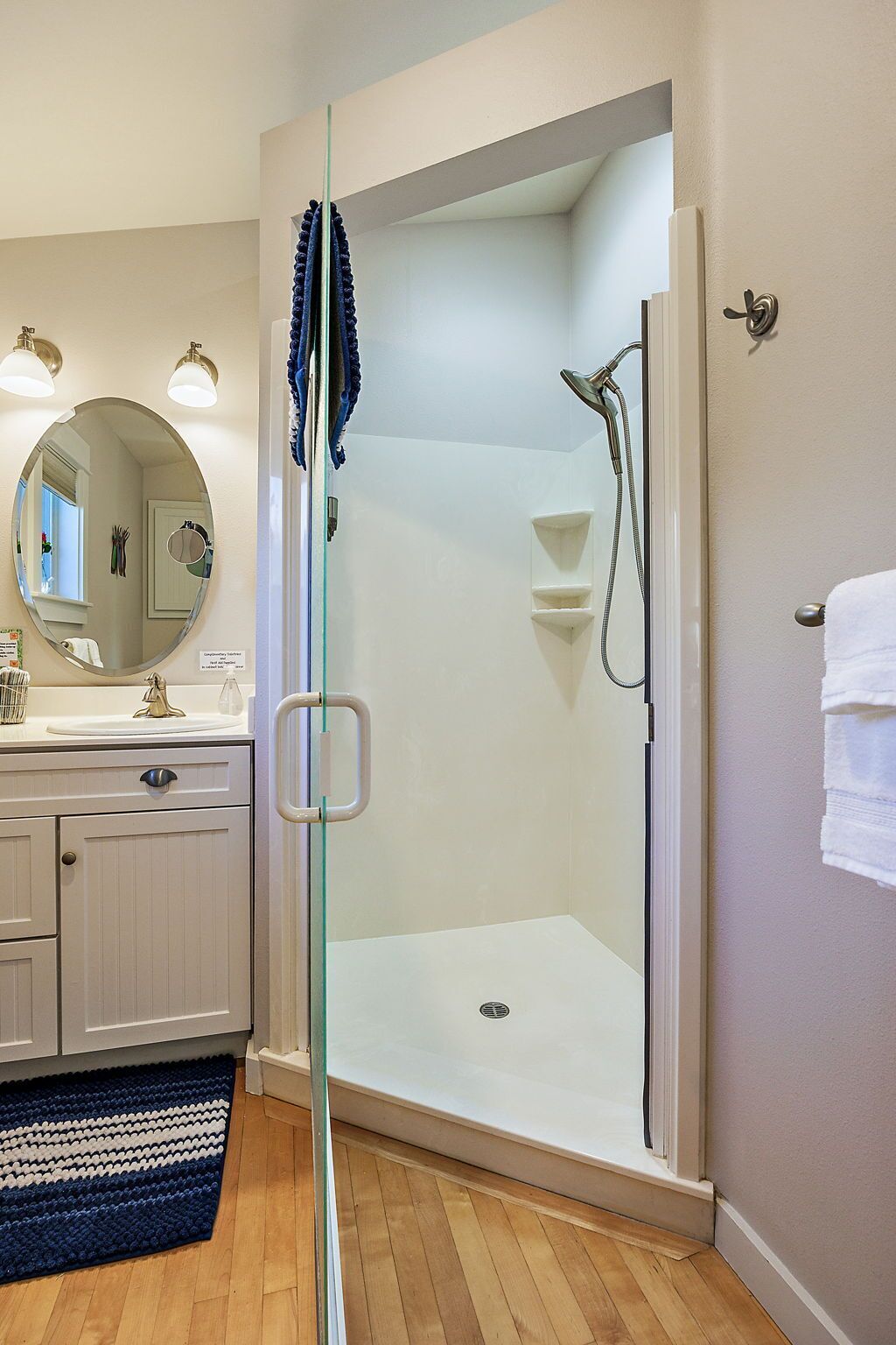 Une salle de bain moderne avec une douche à parois de verre, un meuble-lavabo avec un miroir et un plancher en bois.