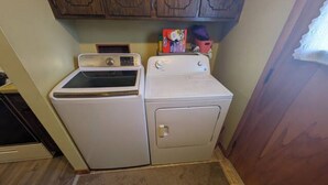 Un espace buanderie équipé d’un lave-linge et d’un sèche-linge à chargement frontal, de placards en bois au-dessus et d’un sol recouvert de moquette.