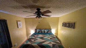 Une chambre à coucher avec un lit, un ventilateur de plafond et deux cadres photo fixés au mur.