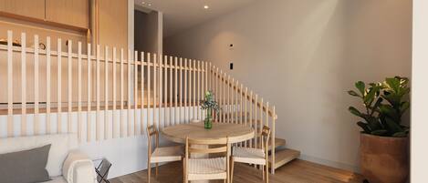 Un espacio de estar moderno con una mesa de comedor redonda de madera rodeada por cuatro sillas, un sofá blanco con cojines y una planta grande en maceta.