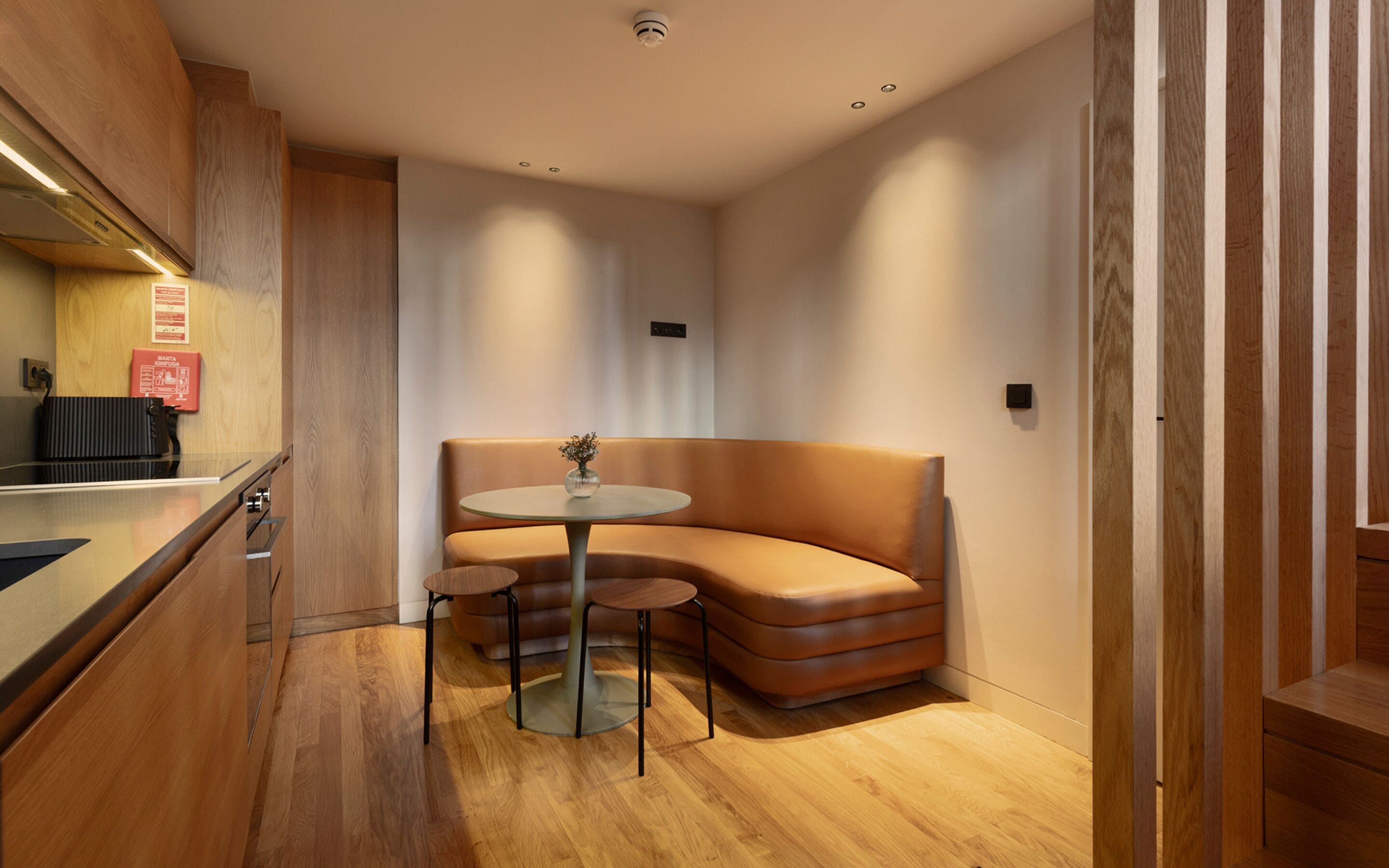 Een moderne kamer met een houten vloer, een ronde tafel met twee stoelen, een comfortabele bank en een klein tafeltje met een vaas.