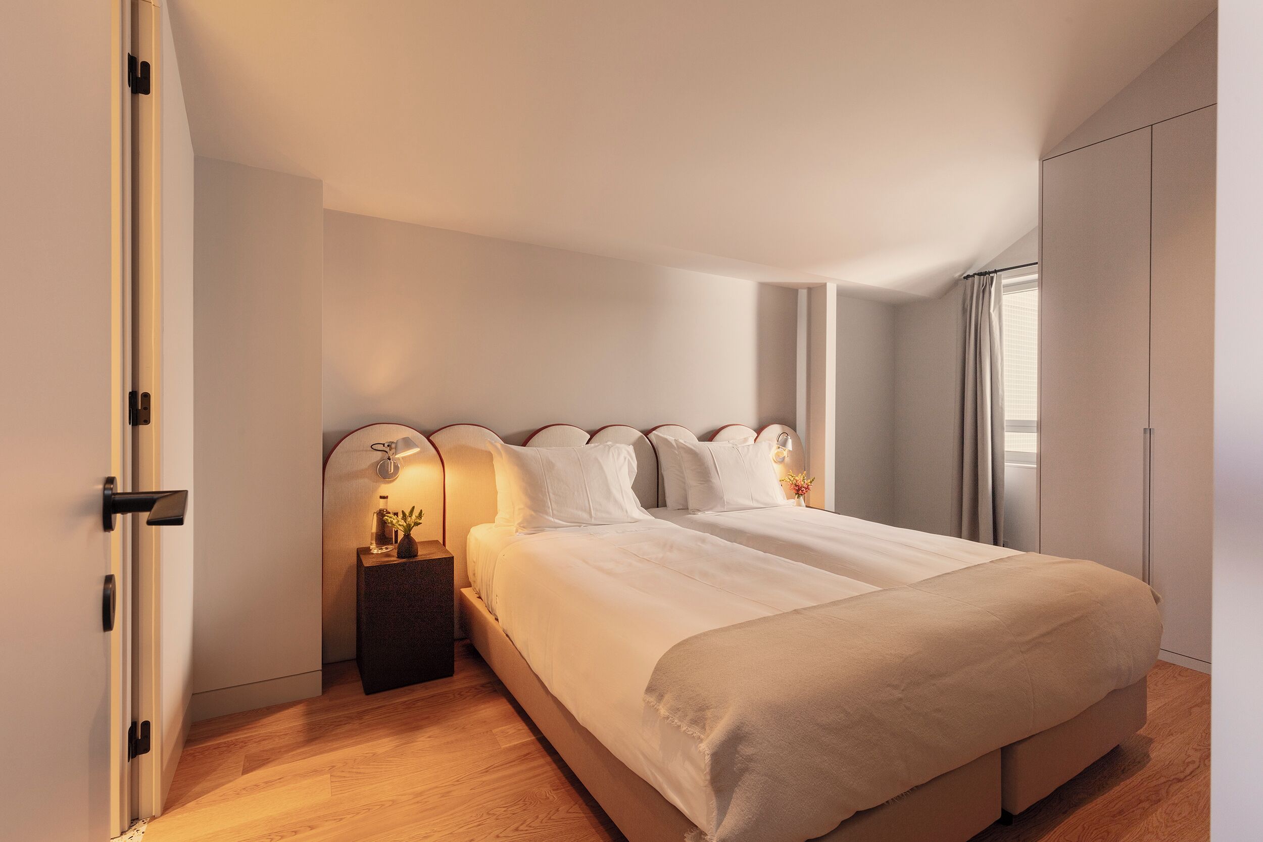 A bedroom with a large bed, a nightstand with a lamp, and a wardrobe.