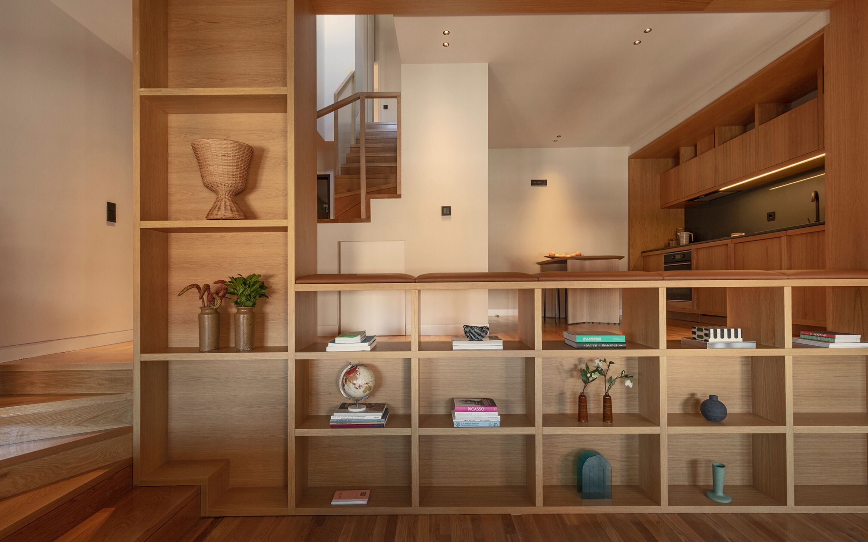 Ein modernes Interieur mit Holzbögen, die Bücher und Dekoartikel präsentieren, einer Treppe und einer Küchenzeile.