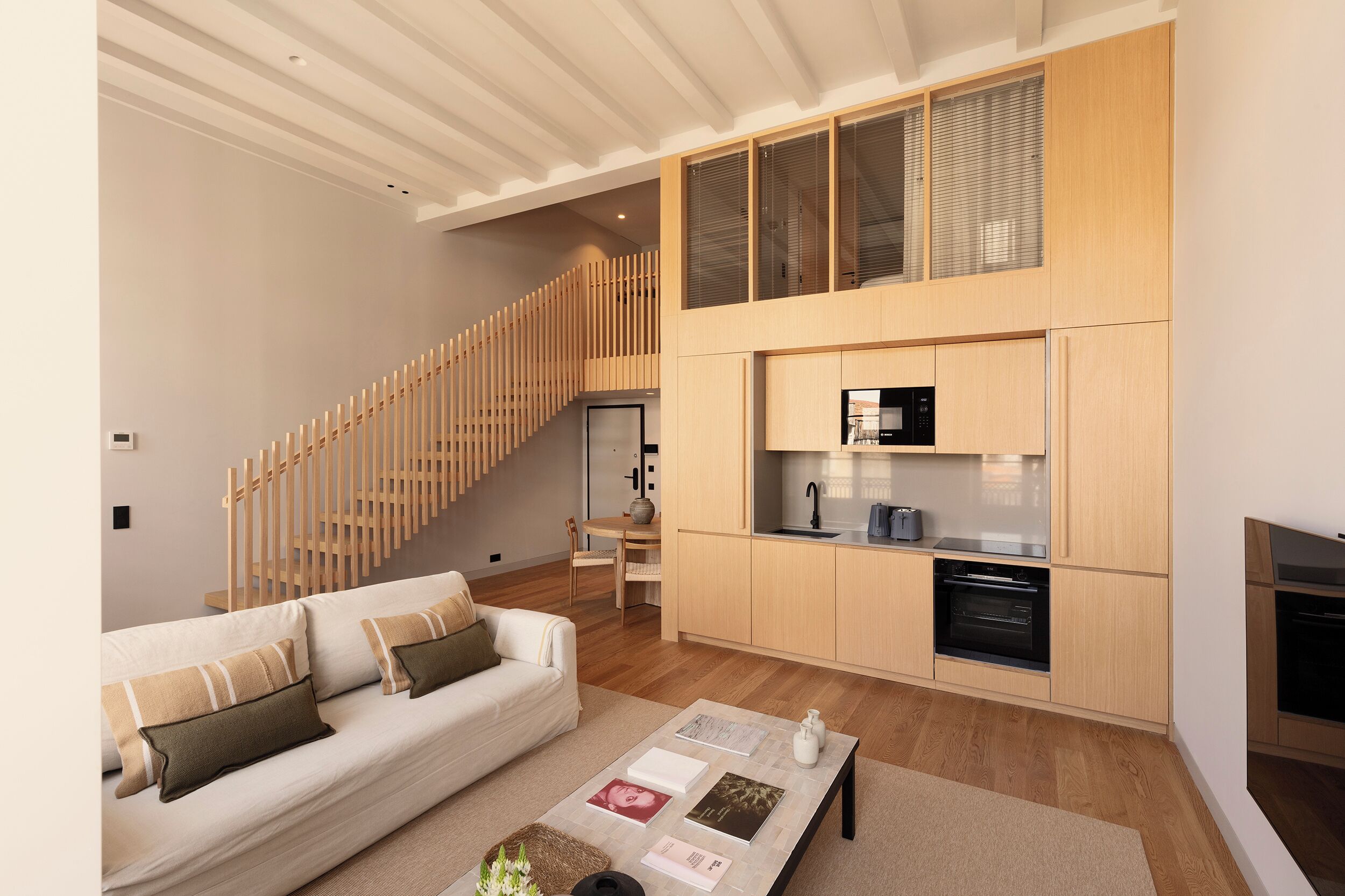 A modern living space with a staircase, a kitchen area, and a seating area with a sofa and coffee table.