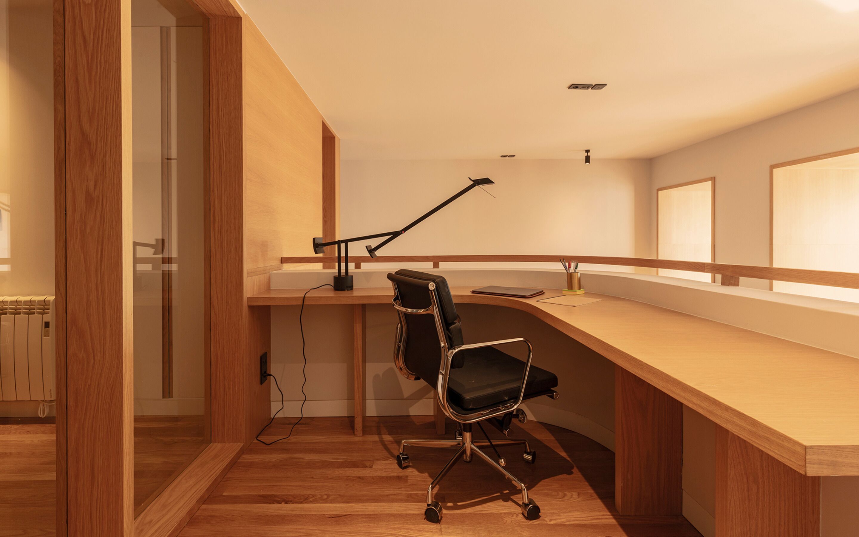 A modern office space with a wooden desk, a black office chair, and a desk lamp.