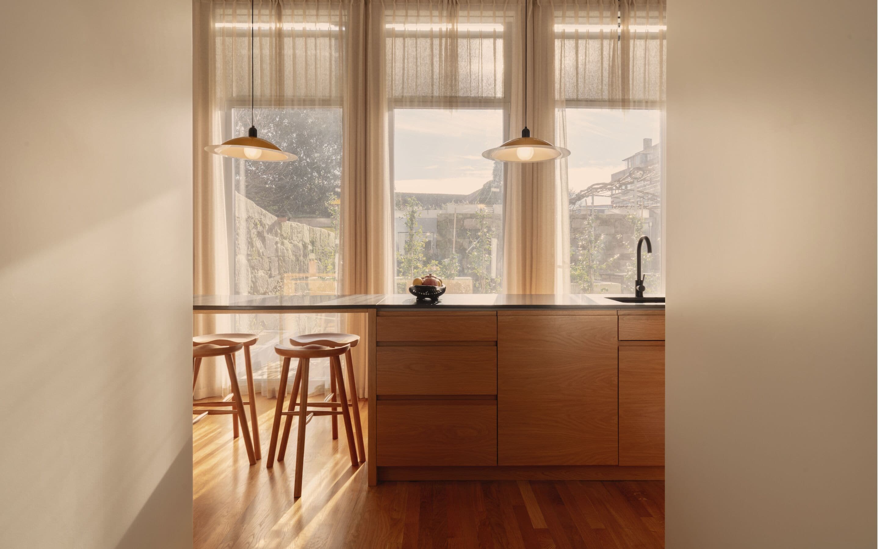 Une cuisine avec des meubles en bois, un évier noir et deux luminaires suspendus.