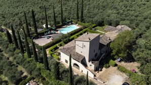 Vista aérea de una propiedad con piscina, un edificio grande y un jardín bien cuidado con árboles altos.