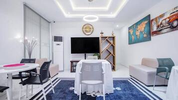 A modern hotel room with a dining area, a large flat-screen TV, a world map painting, and a motorcycle artwork.