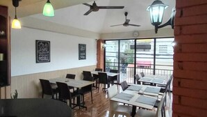 Un comedor interior con piso de madera, mesas, sillas, ventiladores de techo e iluminación colgante.