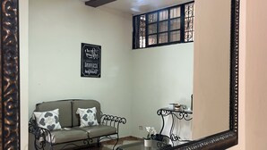 Una sala de estar con un sofá, una mesa de centro, un espejo decorativo y un ventanal con barandales.