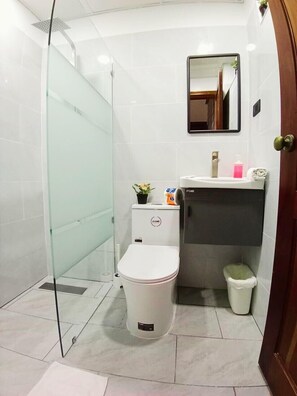 Un baño moderno con cabina de ducha de vidrio, inodoro, lavabo con espejo y un cubo de basura.
