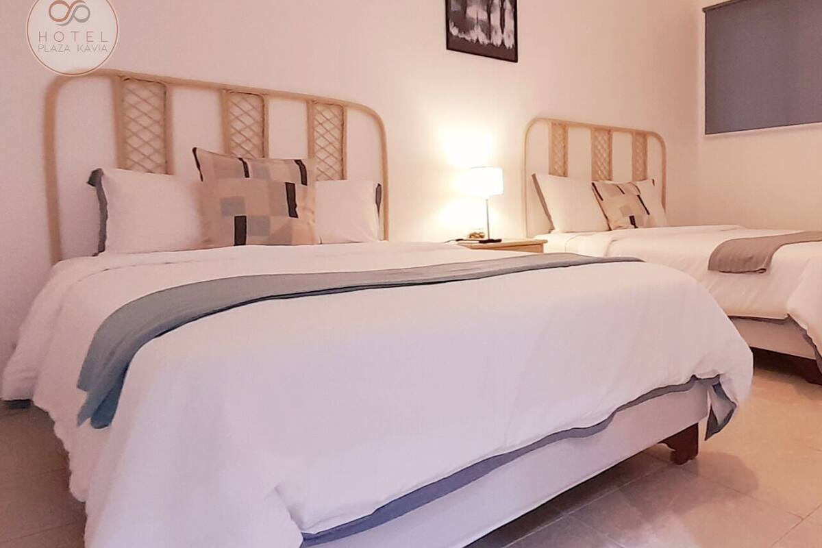 A hotel room with two beds, each with a wooden headboard, white bedding, and a lamp on the nightstand.