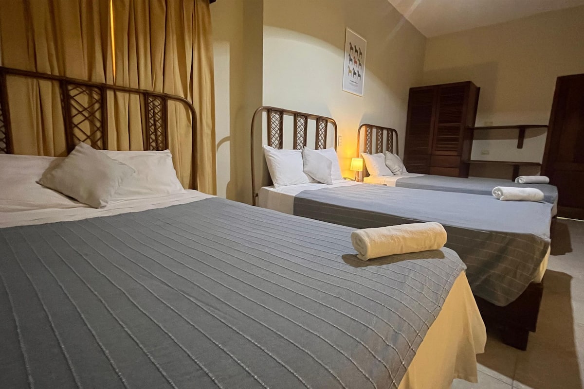 A hotel room with two beds, each with a headboard and pillows. There is a wooden wardrobe and a framed picture on the wall.