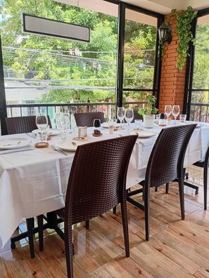 Comedor con una mesa dispuesta para cuatro personas, rodeada de sillas de mimbre, y vista a zonas verdes.