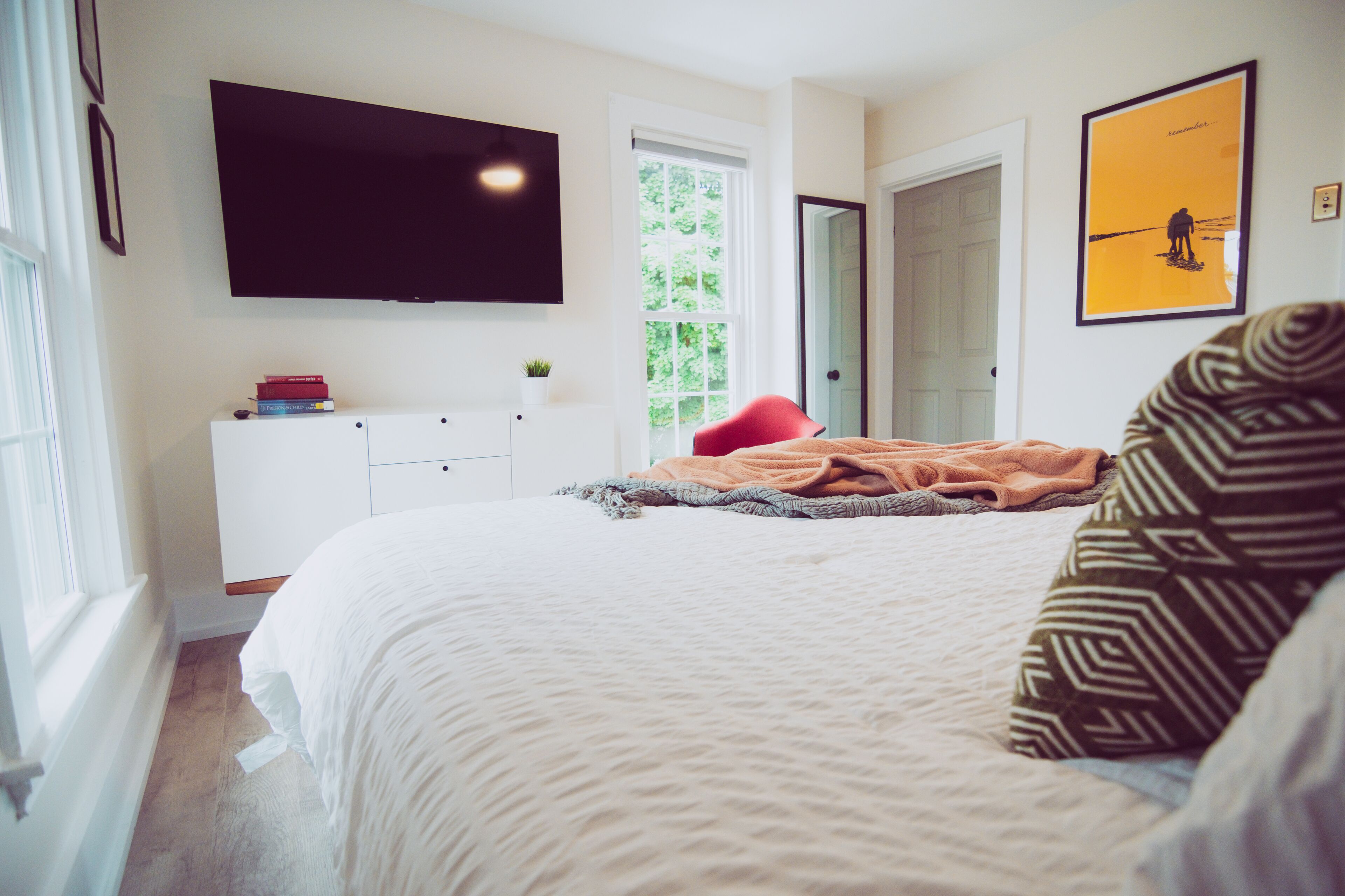Un dormitorio con cama, televisor montado en la pared, puerta y un cuadro enmarcado.