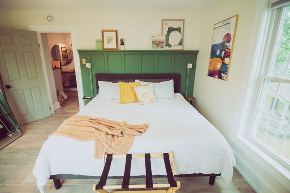Une chambre à coucher avec un lit, un banc, une tête de lit verte et une fenêtre.