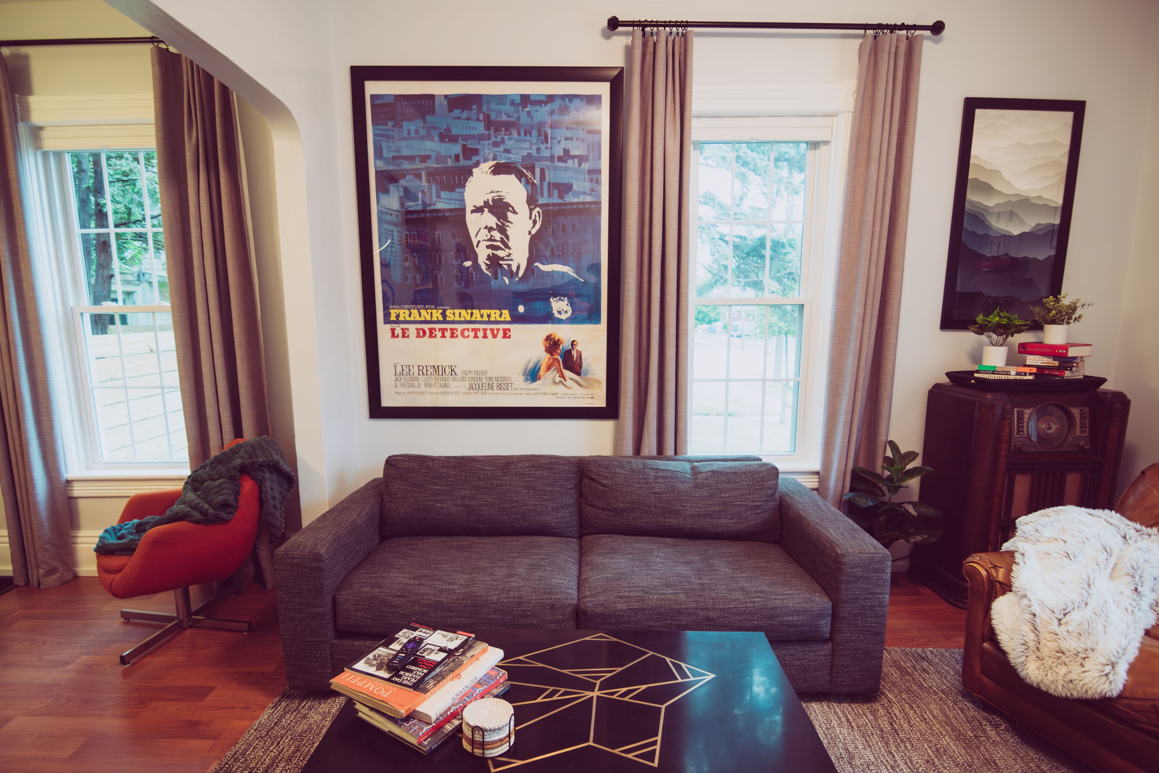 Un soggiorno con un divano grigio, un tavolino da caffè con libri, un poster appeso al muro e una radio su un mobile in legno.