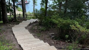 A wooden boardwalk extending through a wooded area with a body of water in the background. - Lake Jocassee Home - Incredible Dock and Mountain and Sunset Views - Devils Fork (Salem)