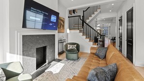 A modern living room with a fireplace, a large TV screen, a staircase, and a sofa with cushions. - The Adams | West Elm 5BR Townhouse in Bloomingdale (Washington)