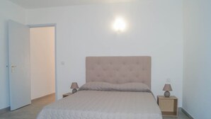 Quarto com cama, duas mesas de cabeceira com abajures, uma porta e um luminário no teto.